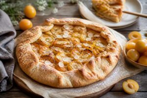 Rustikale Mirabellen-Galette mit Mandelcreme auf einem Holzbrett, goldbraune Ränder, frische Mirabellen als Belag, Spätsommer-Stimmung