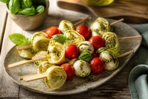 Tortellini-Spieße mit grünem Basilikumpesto, Kirschtomaten und Mini-Mozzarella auf einem Holzbrett beim Grillbuffet